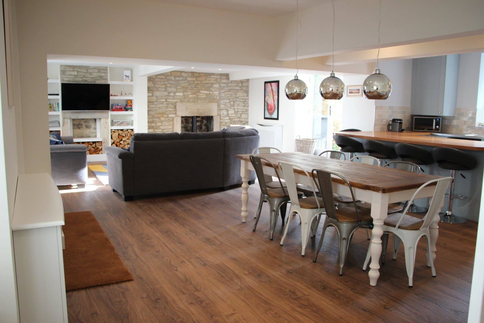 Dining table, breakfast bar, sofa, wall-mounted TV and stone fireplace wall