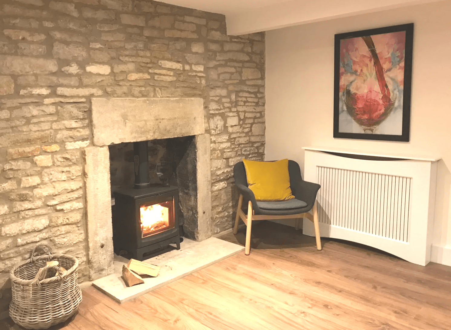 Log burner alight in the stone fireplace, with armchair and log basket