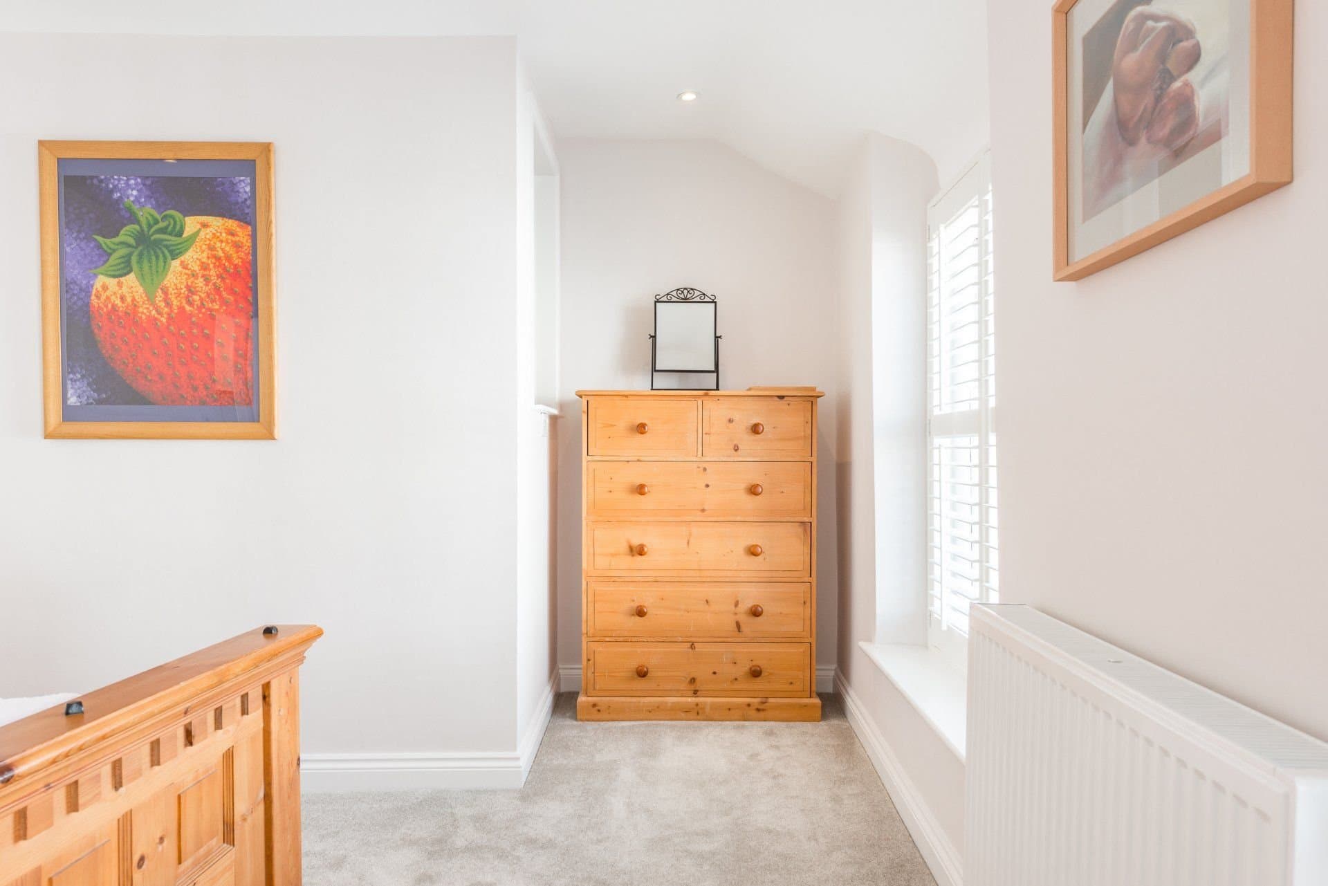 Bedroom corner with a wooden chest of drawers and shutters