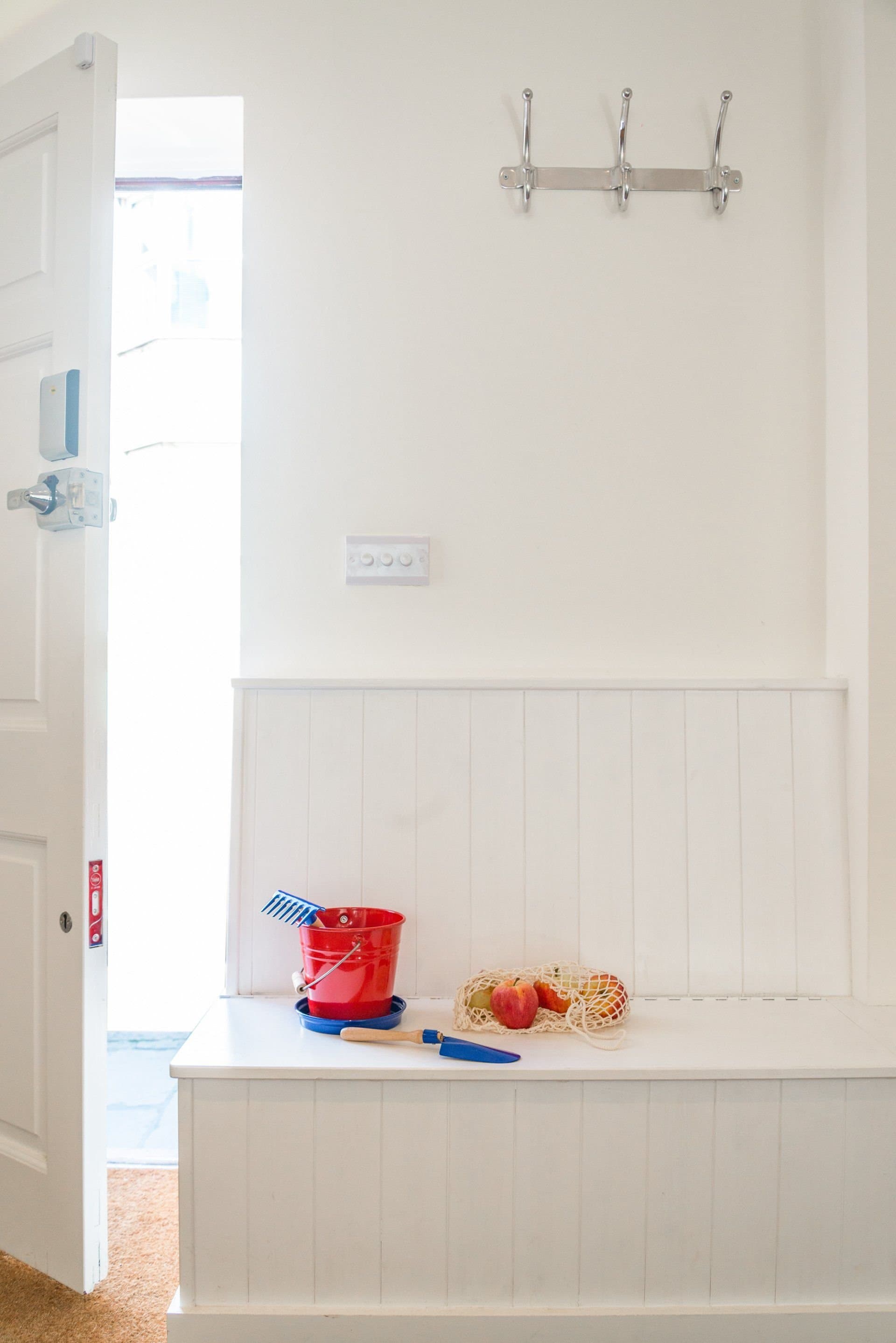 Bright entrance hall with a storage bench, beach bucket and an open front door